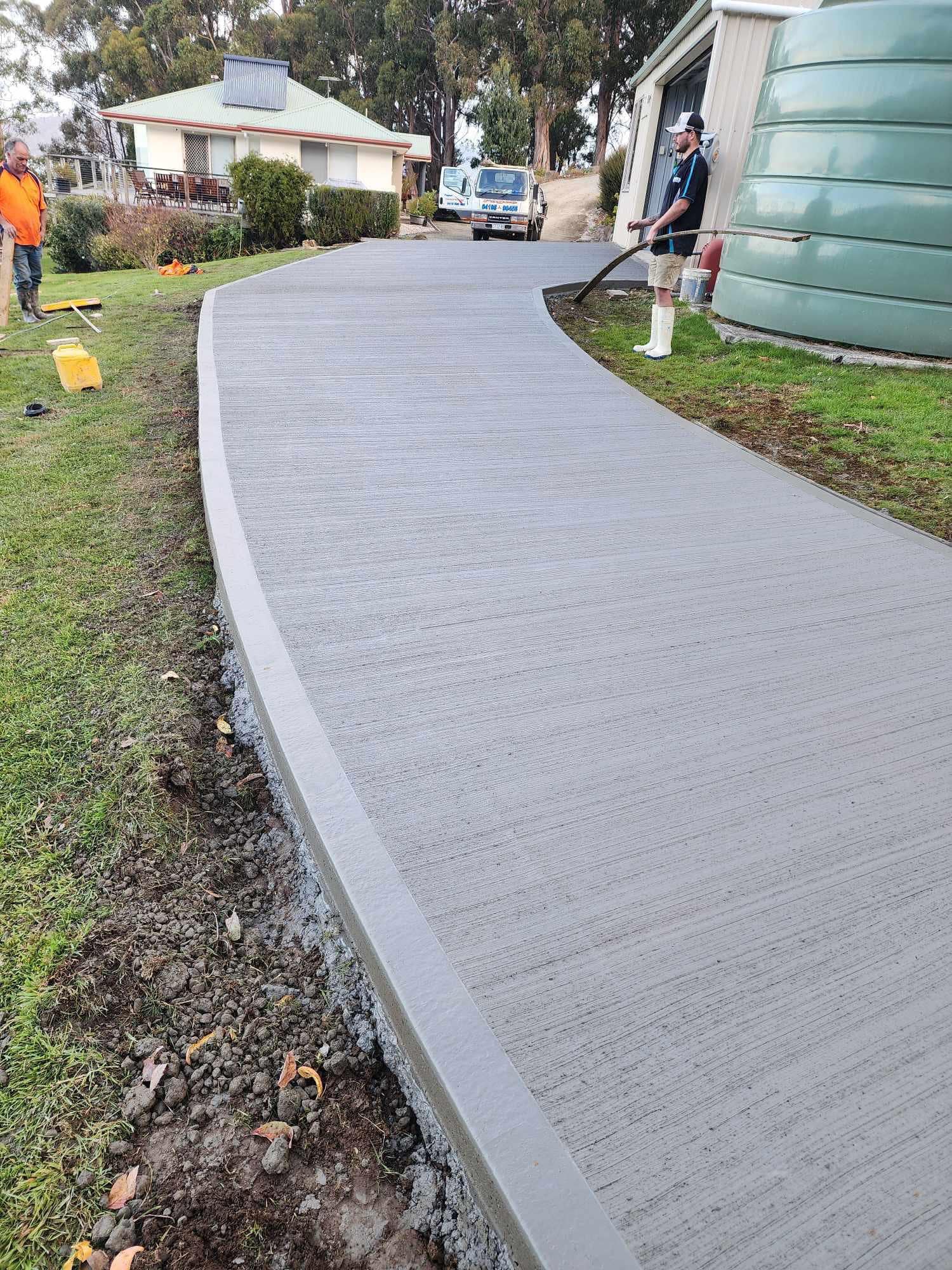 Curved broom-finished concrete driveway and path beside a rural Tasmanian homestead, pump hose visible